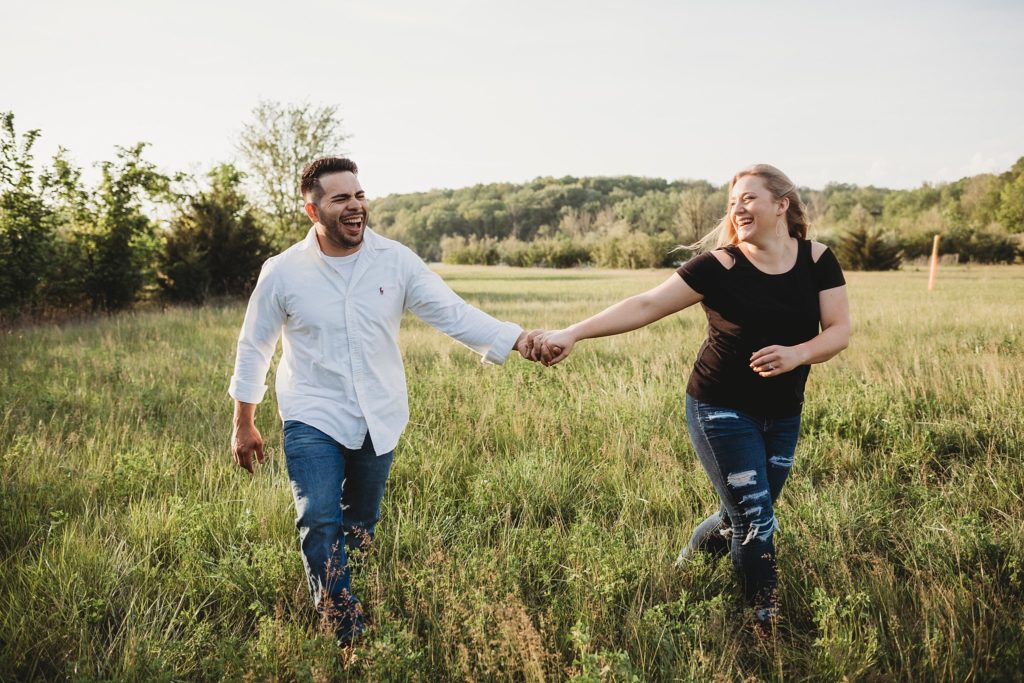 man and woman hold hands and take romantic engagement photos at Fairfield Lakes Park during sunset