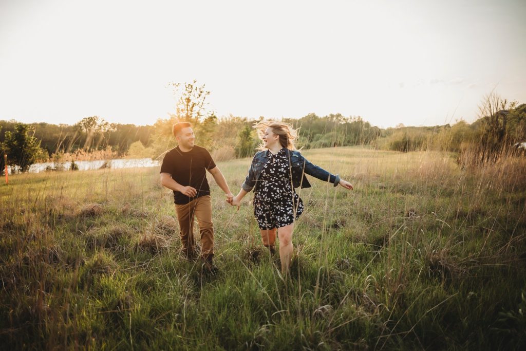 man and woman hold hands and take romantic engagement photos at Fairfield Lakes Park during sunset