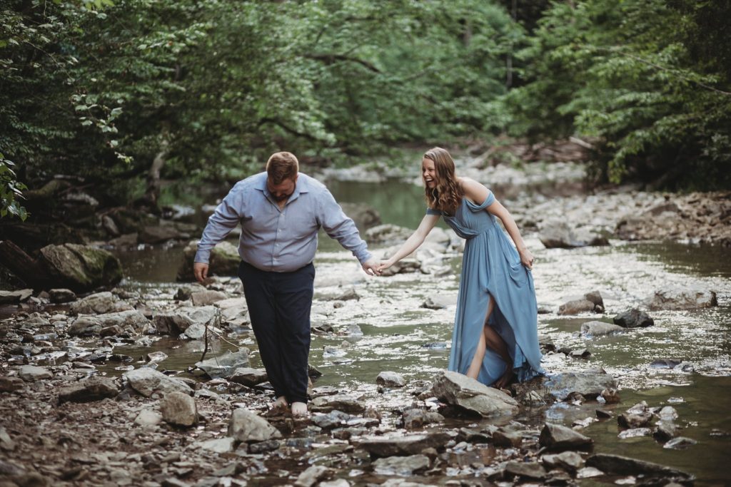 McCormick's Creek Engagement Session- Man and woman holding hands walking across the water at McCormick's Creek State Park in Indiana