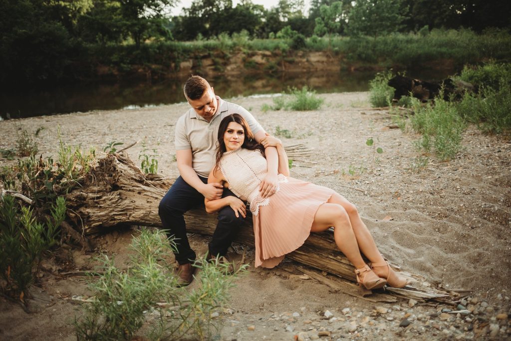 Fairfield Lakes Park Engagement Session- woman laying on man while sitting on a log near water in Lafayette Indiana at Fairfield lakes park.