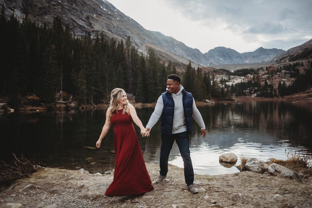 Breckenridge Engagement Session-couple holding hands by lake and mountains in colorado