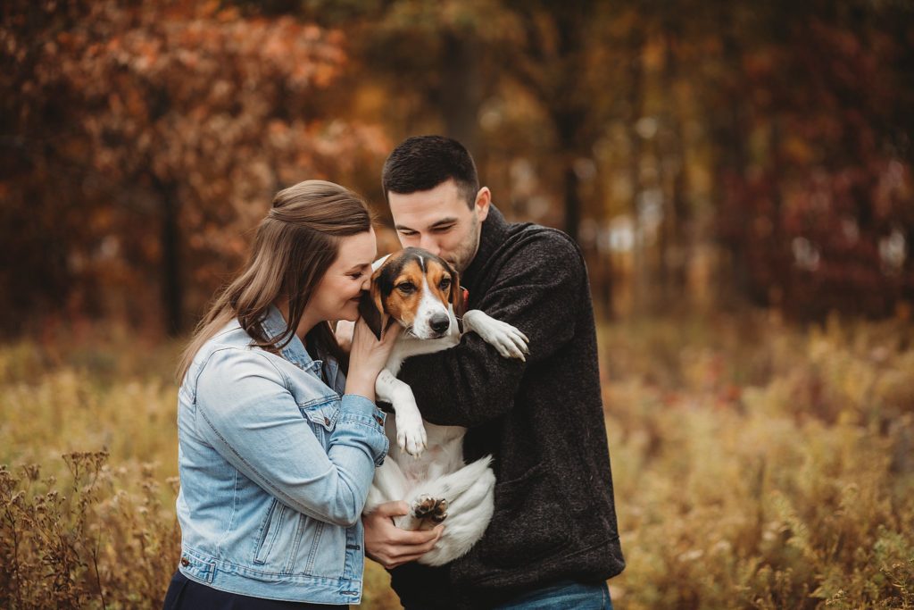man and woman cuddling their dog in a park