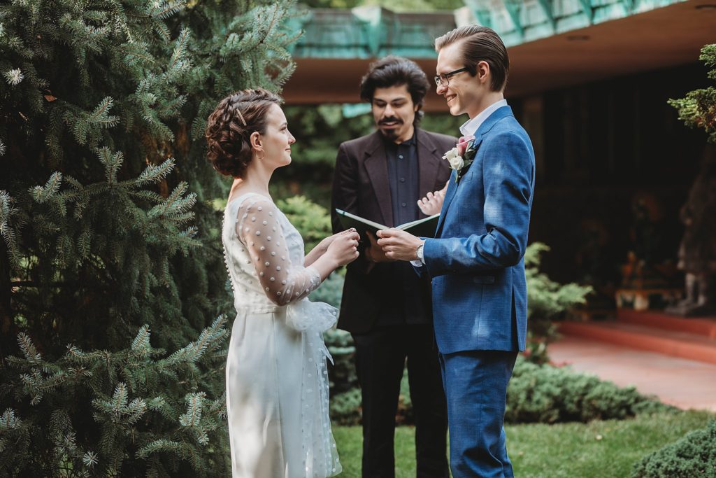 bride and groom exchange rings in front of the samara house