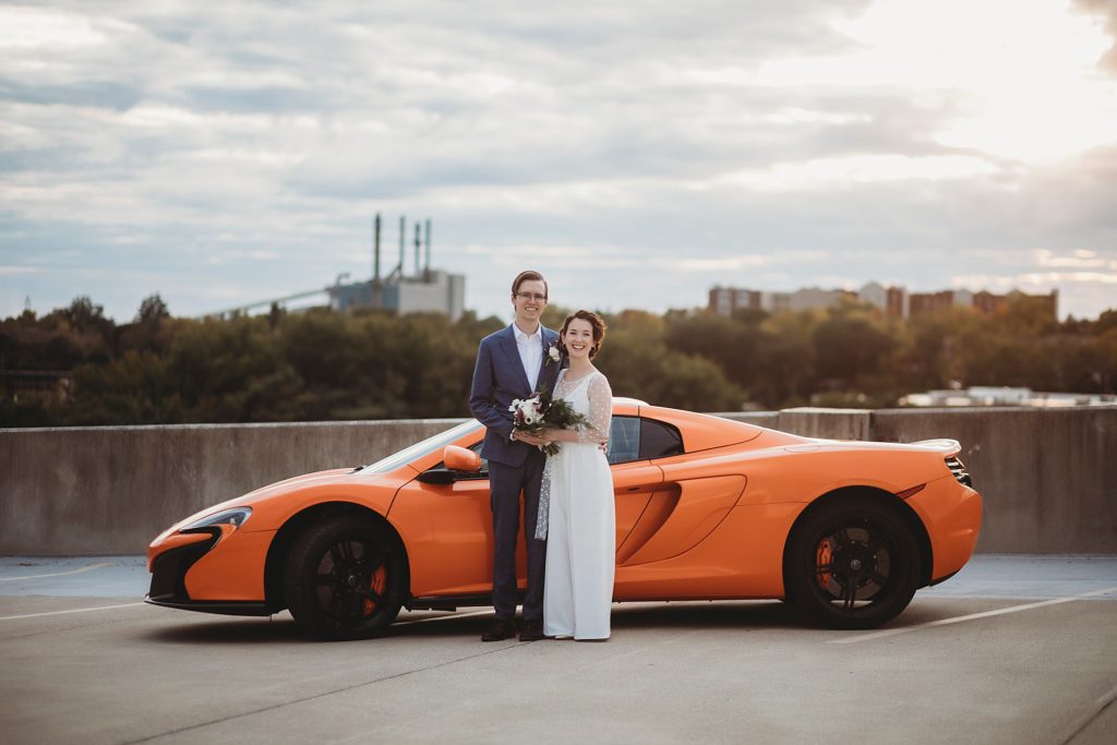 bride and groom pose in front of foreign car