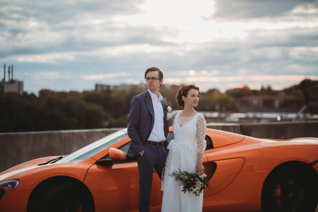 bride and groom pose in front of foreign car in west Lafayette Indiana