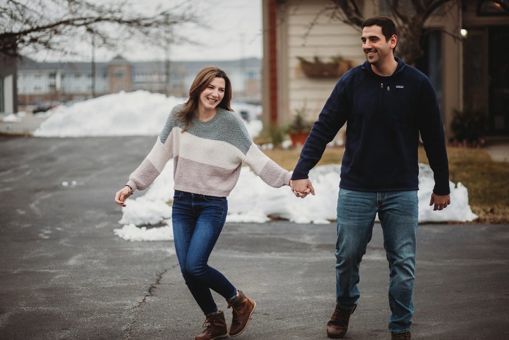 Man holding woman's hand while they are walking in front of their home at their Crown Point Indiana Engagement Session