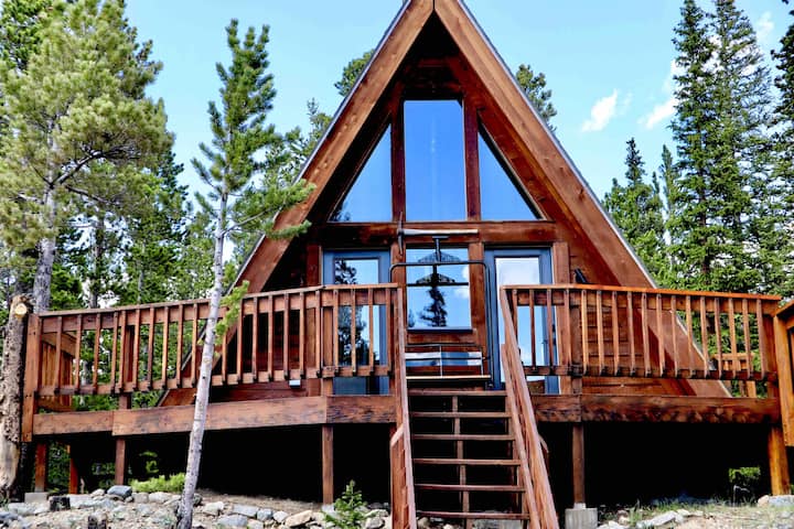 Best Colorado A-Frames- A-Frame Cabin in Idaho Springs, Colorado surriounded by trees and a blue sky.