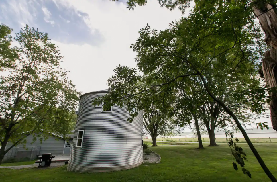 Indiana Airbnb that looks like a grain bin. Trees surround the grain bin with lush green grass. 