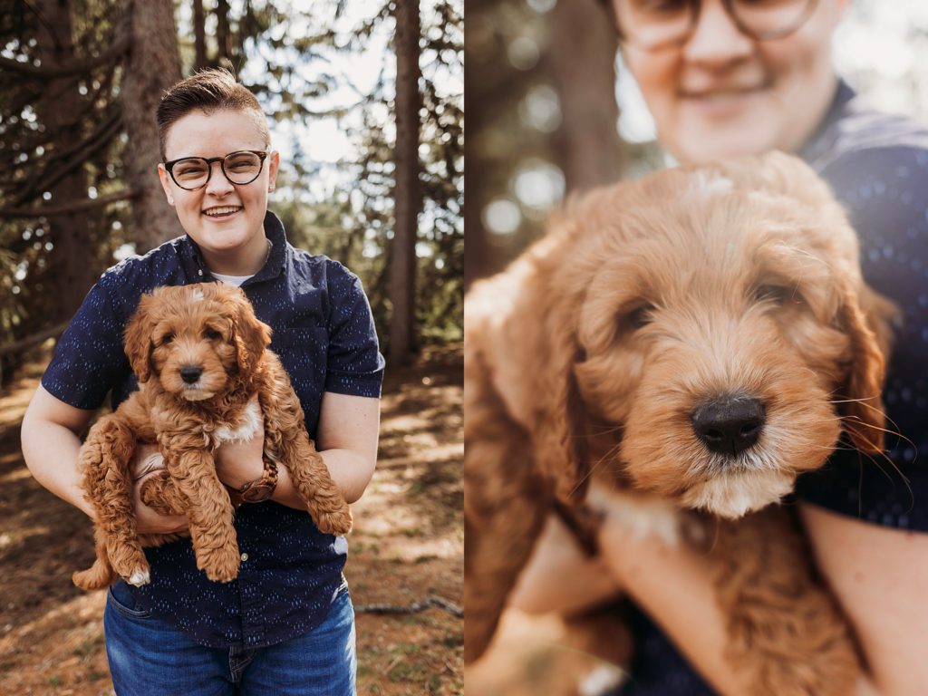 Person in blue shirt smiling at camera while holding golden puppy in arms.