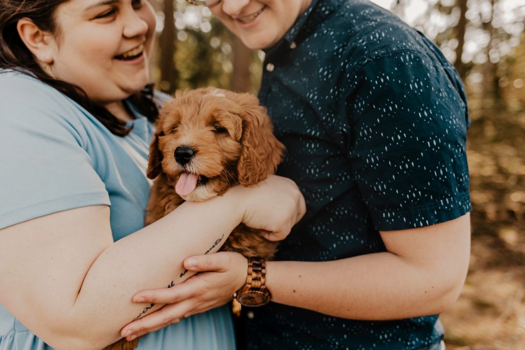 couple holds golden puppy in arms while smiling and looking down at it at Purdue horticulture park