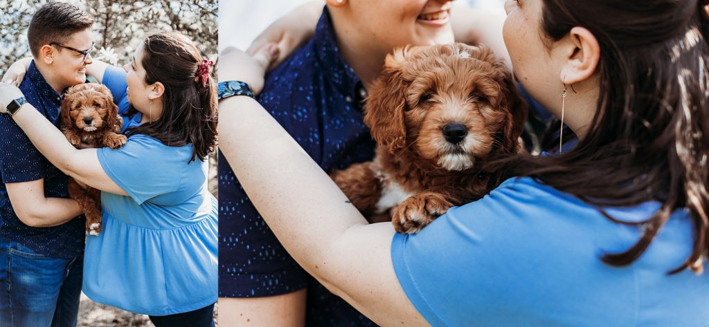 couple holding onto one anothr while smiling at eachother and puppy looking at the camera while perked up in between them