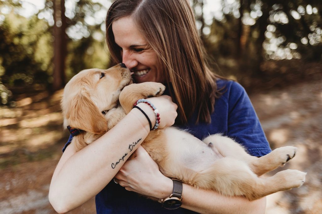 Girl in blue shirt holding puppy with noses touching.