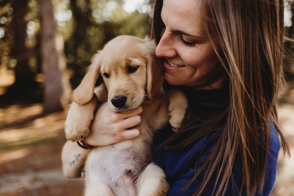 Girl in blue shirt holding golden puppy while looking down at it.
