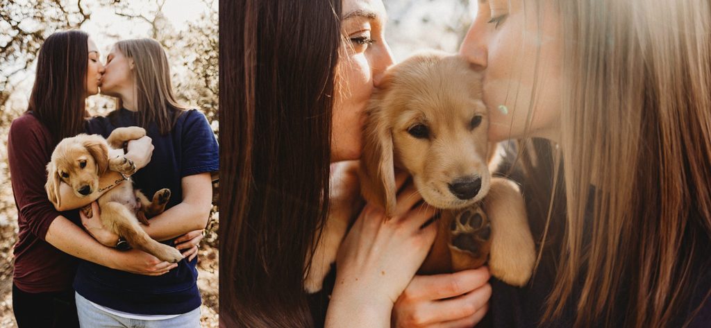 girl in red shirt holding girl in blue while holding puppy in arms while kissing eachother.