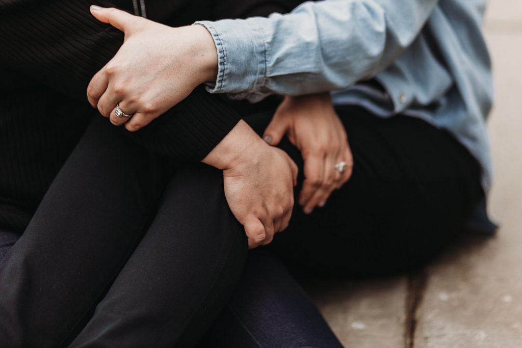 couple's hands and legs held together while showing off engagement rings