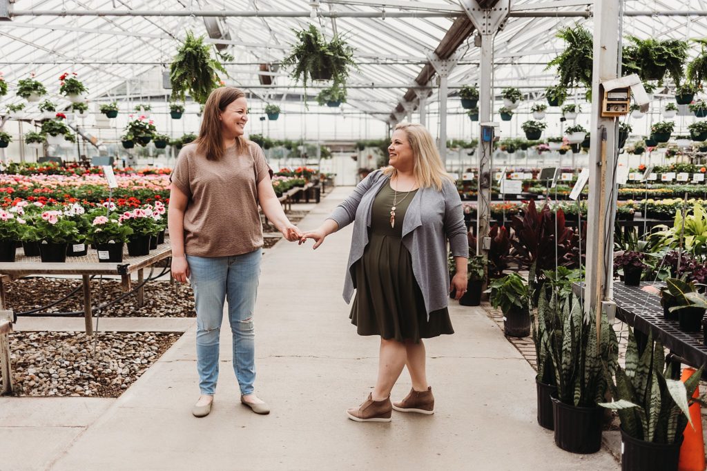 couple holding hands while standing in the middle of indiana greenhouse