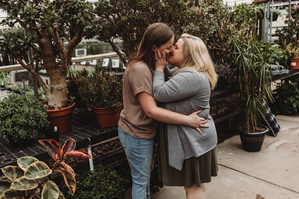 couple holding one another while kissing in front of green and exotic plants