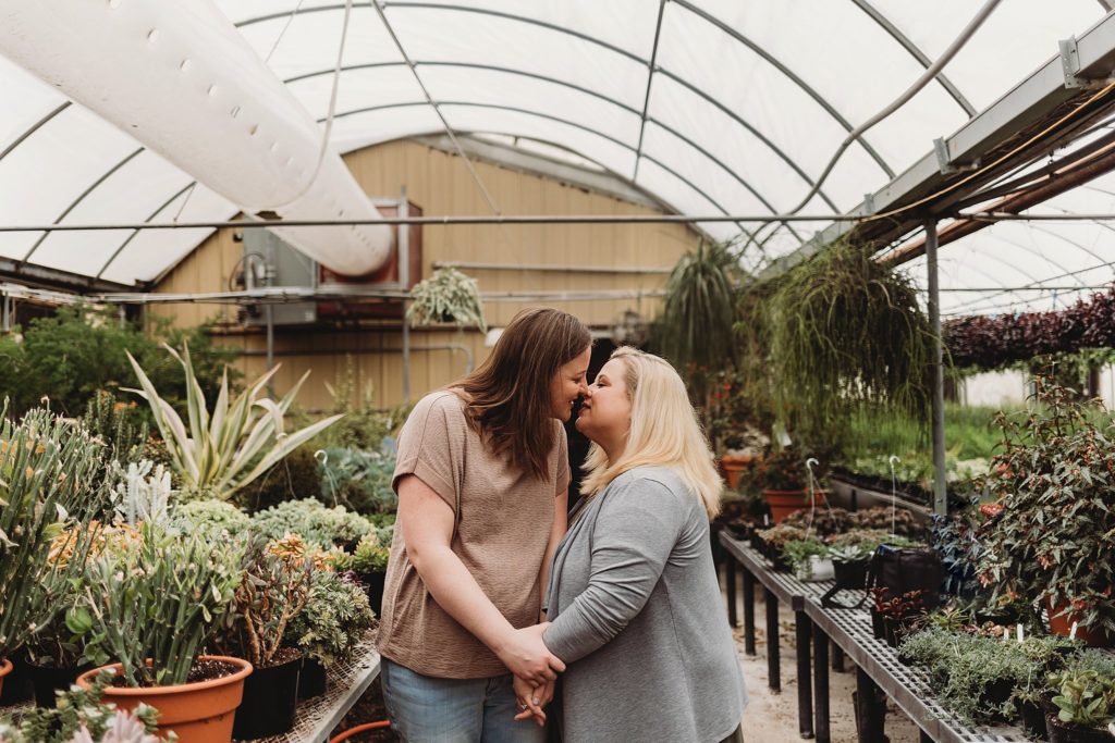 landscape shot of the couple holding hands and getting ready to kiss at each other n the indiana greenhouse