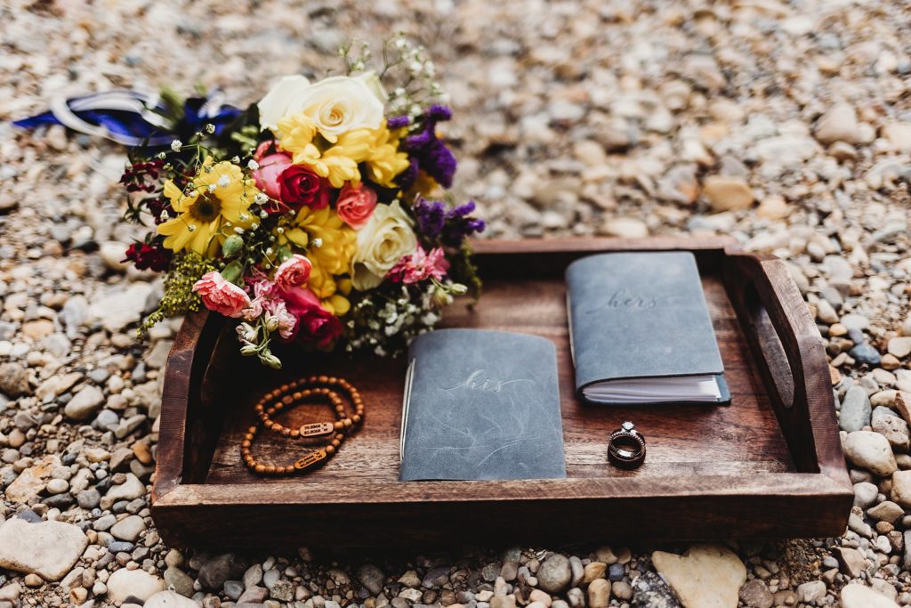 Indianapolis Indiana Elopement- flowers, bracelets, vow books, and rings sitting on a tray on a river bank at an Indianapolis, Indiana Elopement