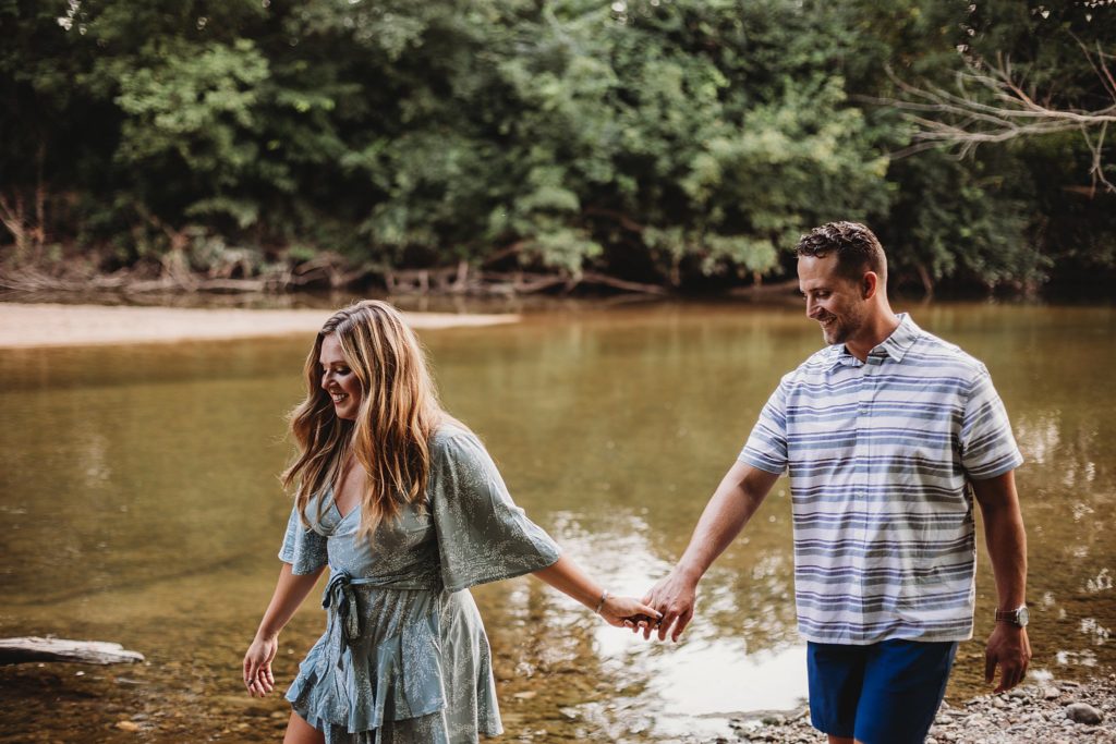 man and woman walk beside Wildcat Creek at their Indiana Couples Session in lafayette, Indiana at Fairfield Lakes Park