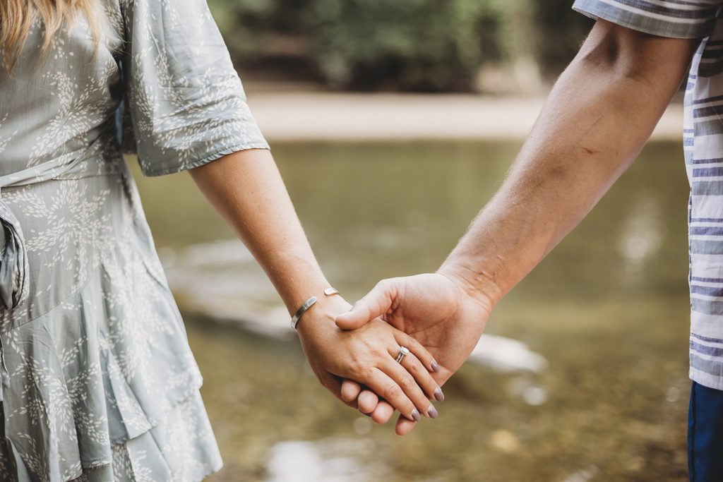 man and woman hold hands beside Wildcat Creek at their Indiana Couples Session in lafayette, Indiana at Fairfield Lakes Park