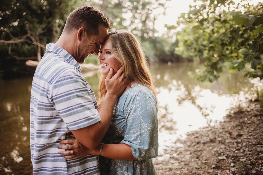man and woman lean their heads together beside Wildcat Creek at their Indiana Couples Session in lafayette, Indiana