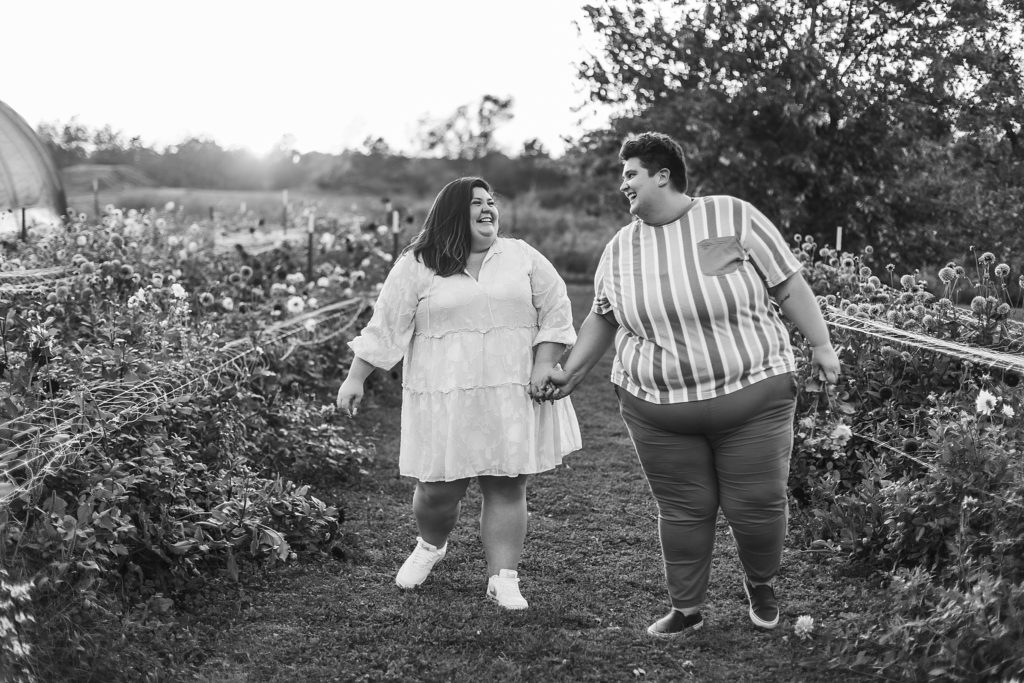 21 Petals Engagement Session- Two women hold hands while walking through a flower field at 21 Petals in Lafayette, Indiana