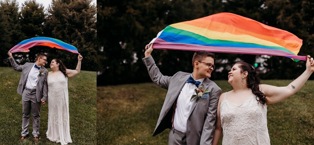 wife and wife holding hands and holding onto a rainbow pride flag that is blowing in the wind at their LGBTQ Wedding venue 