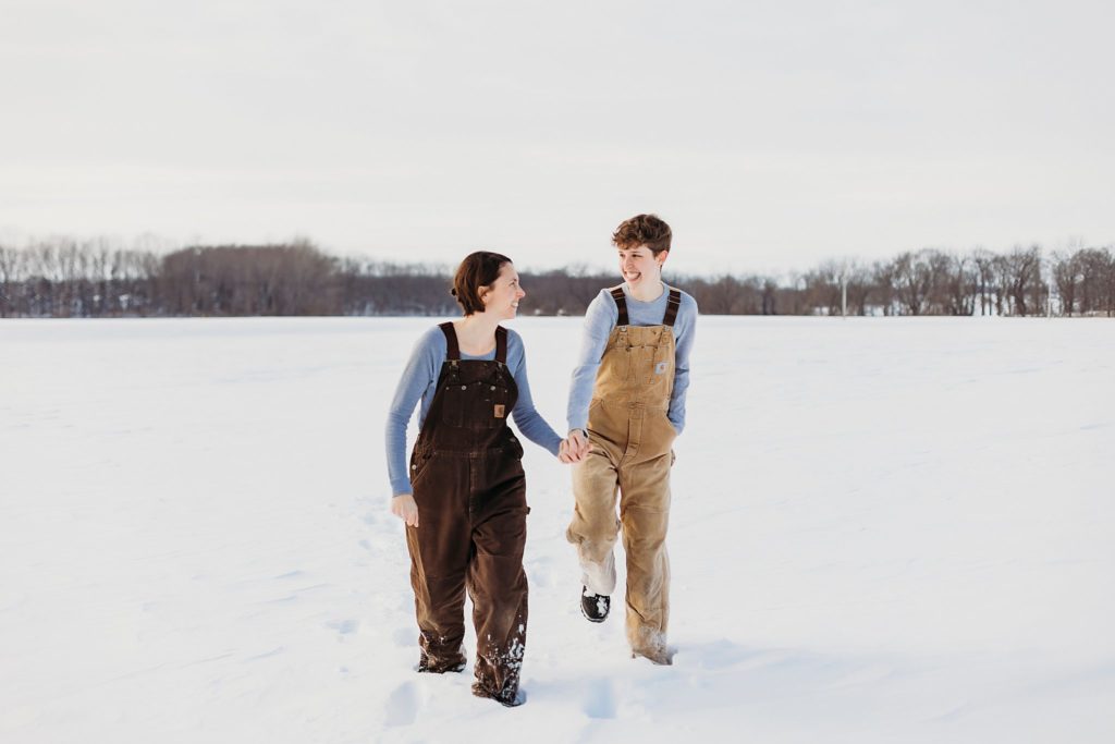 women running the middle of a snow covered field during their indiana winter engagement session