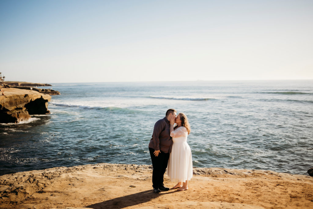 couple kissing on a large rock at sunset cliffs in san diego california in front of the ocean at their california elopement