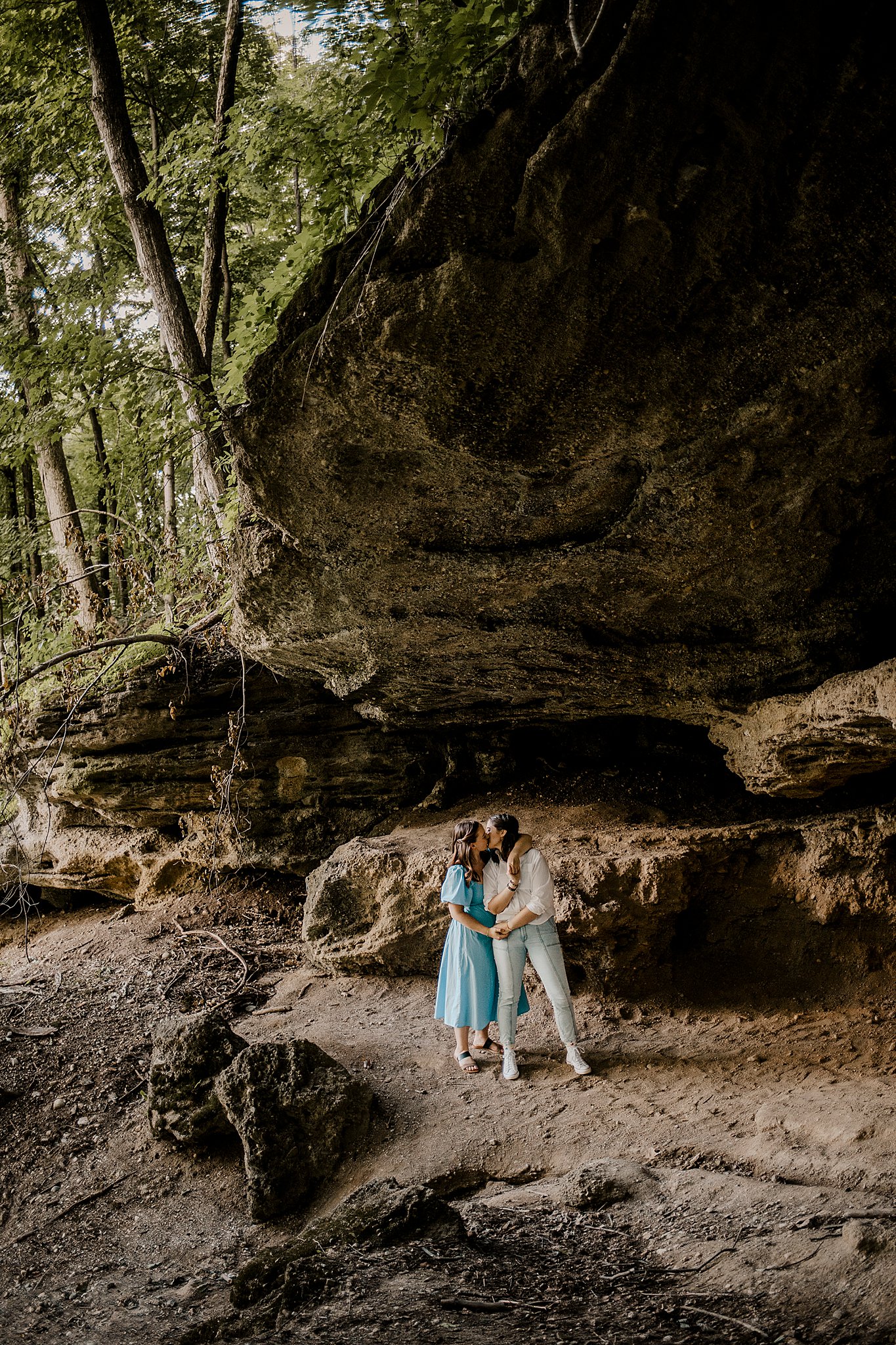 Samantha Mitchell, an LGBTQ Engagement photographer captures two women at Prophet's Rock in Indiana. The two women are snuggling together amongst large rocks. They are laughing and smiling at one another.