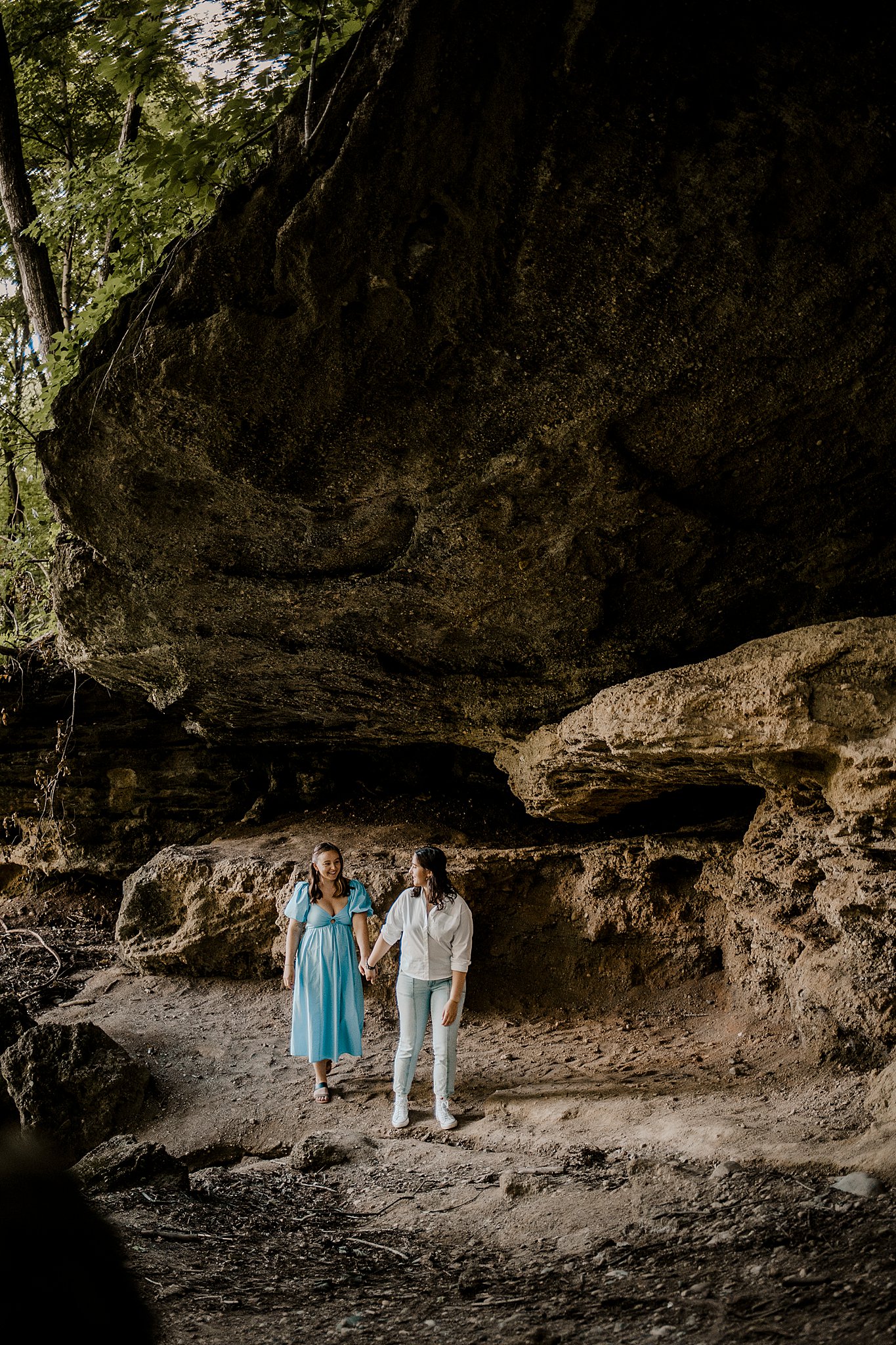 Samantha Mitchell, an LGBTQ Engagement photographer captures two women at Prophet's Rock in Indiana. The two women are snuggling together amongst large rocks. They are laughing and smiling at one another.