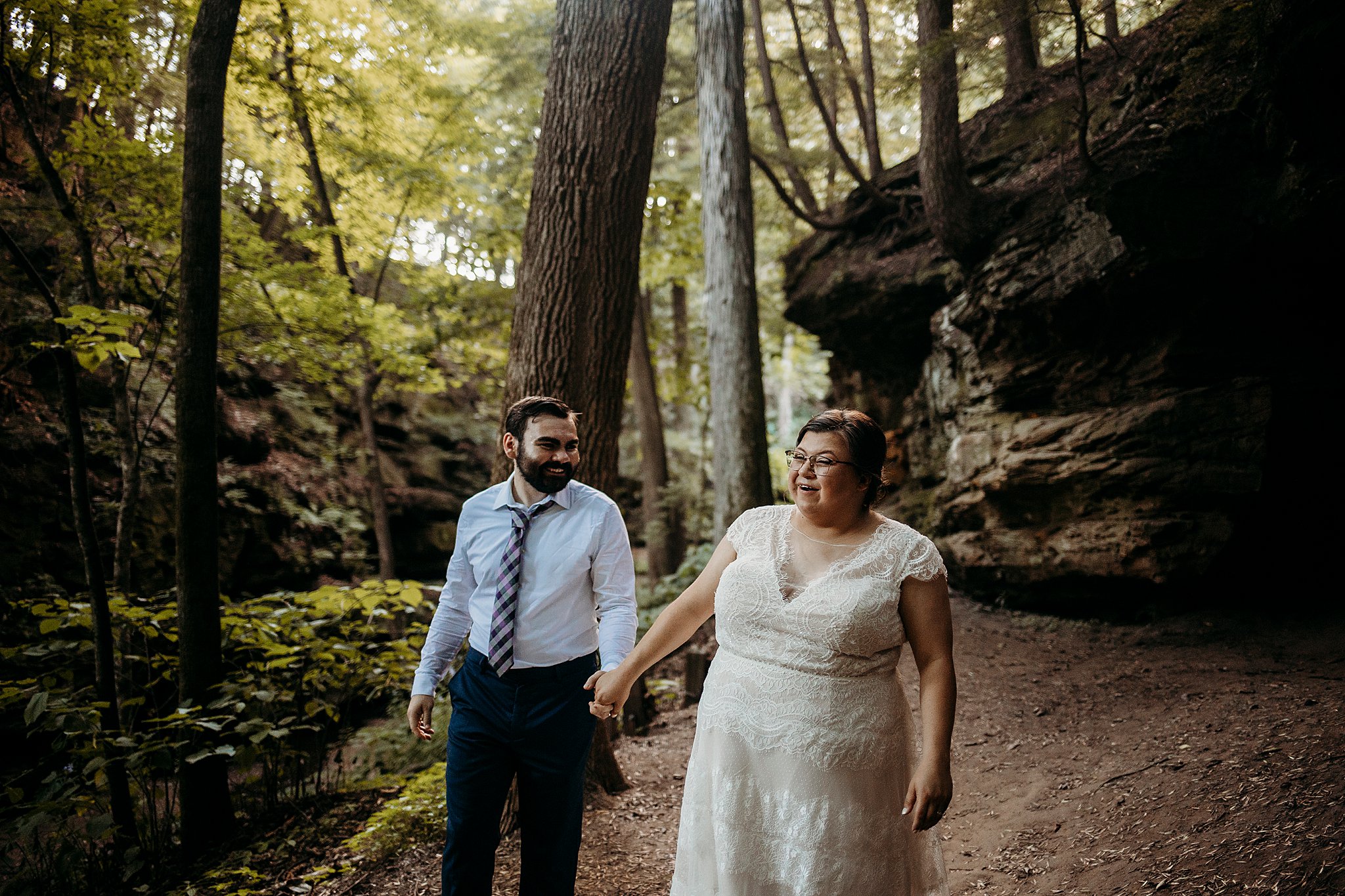 A man and a woman hold hands while smiling at each other while being surrounded with large rock and big trees at their Turkey Run Elopement