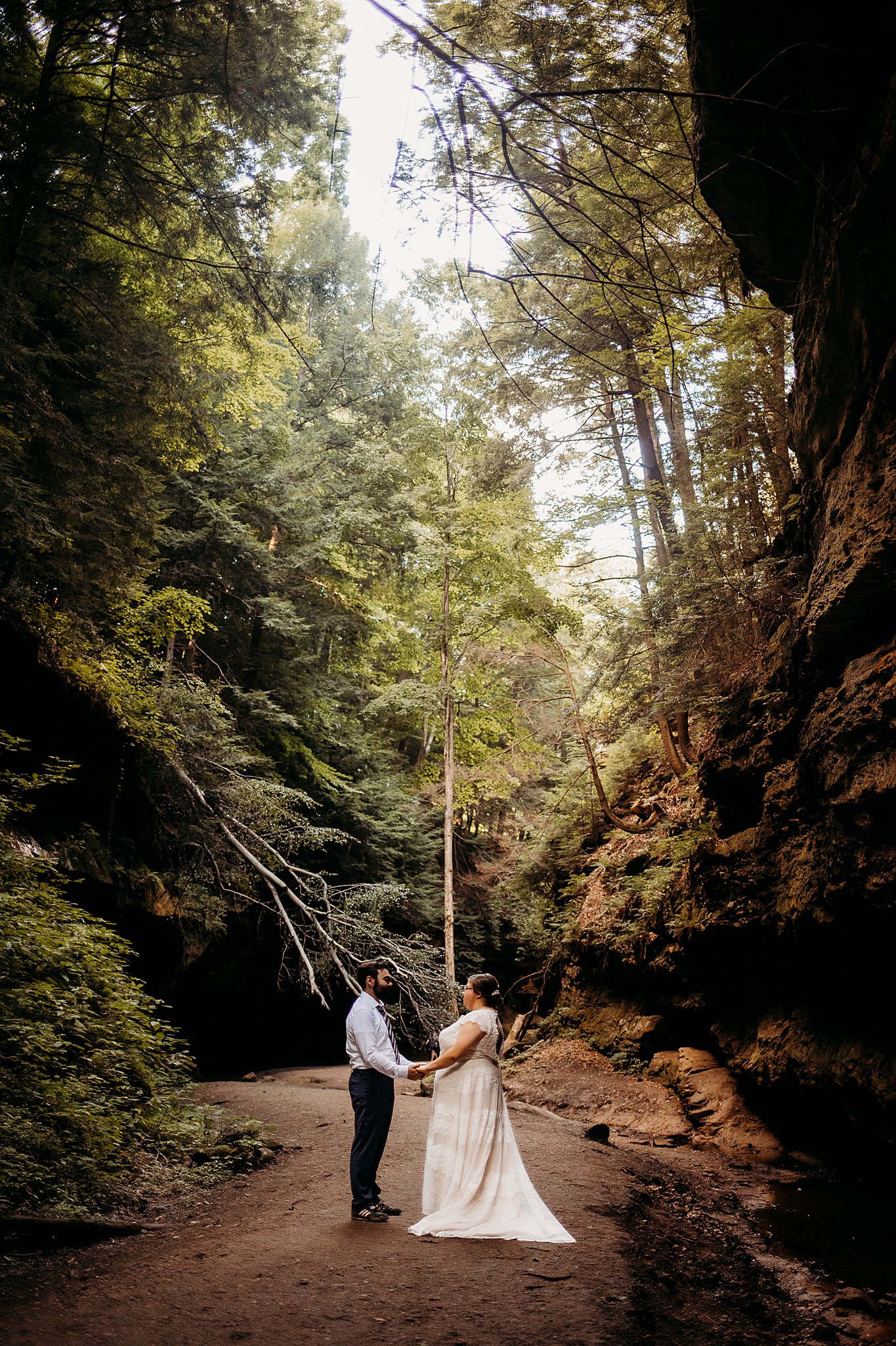 A man and a woman hold hands while being surrounded with large rock and big trees at their Turkey Run Elopement