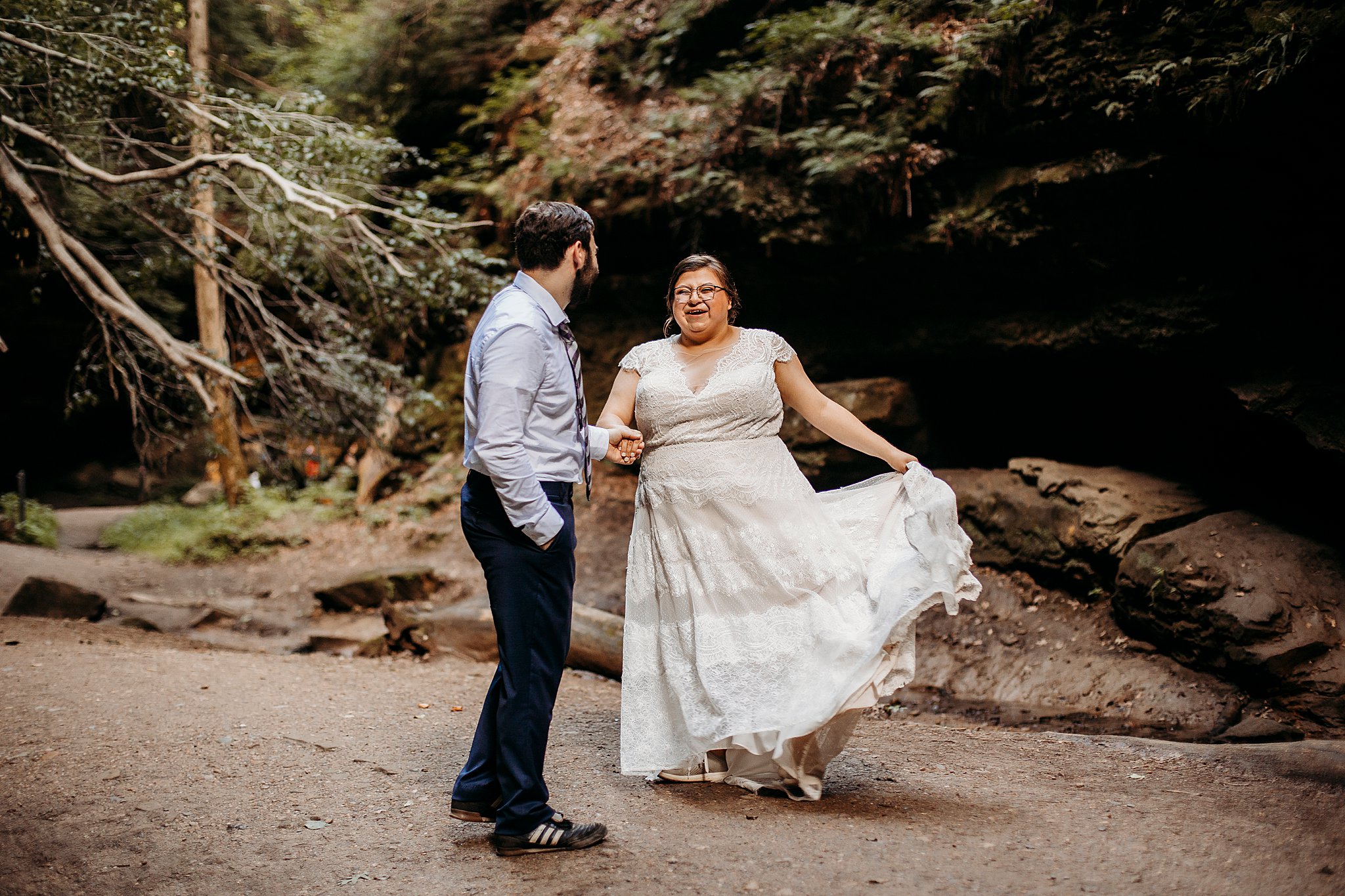 A man and a woman hold hands and dance while being surrounded with large rock and big trees at their Turkey Run Elopement