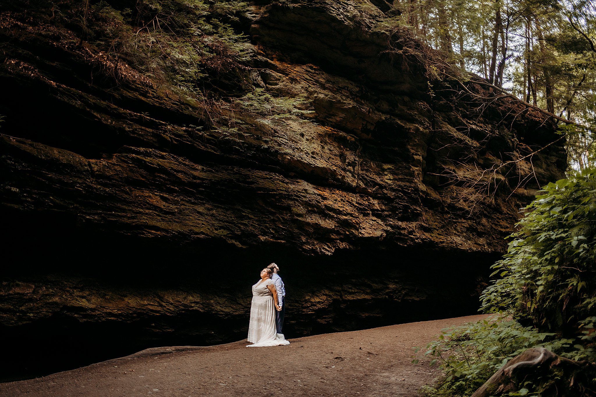 A man and a woman stand back to back while being surrounded with large rock and big trees at their Turkey Run Elopement