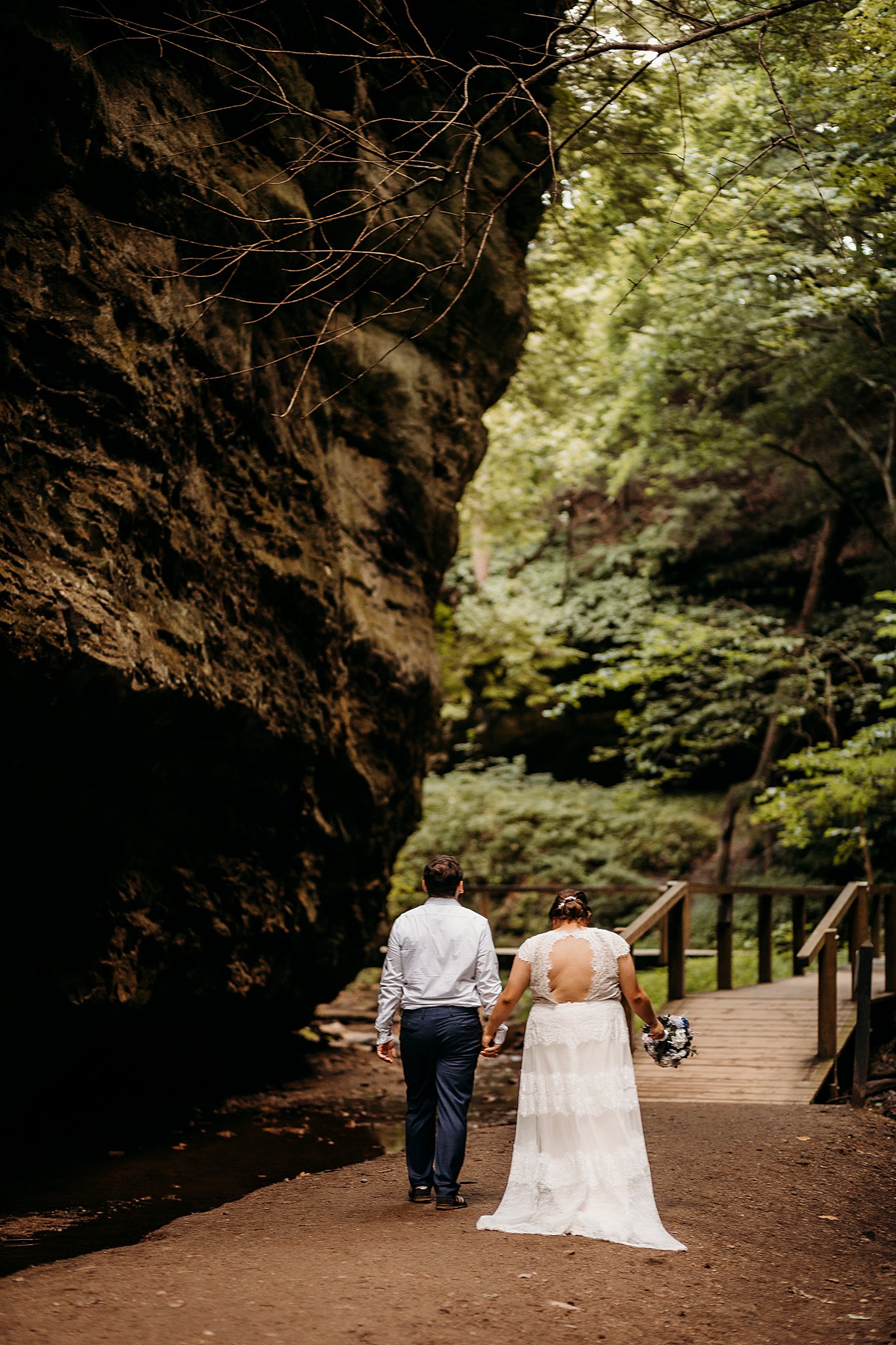 A man and a woman hold hands while being surrounded with large rock and big trees at their Turkey Run Elopement