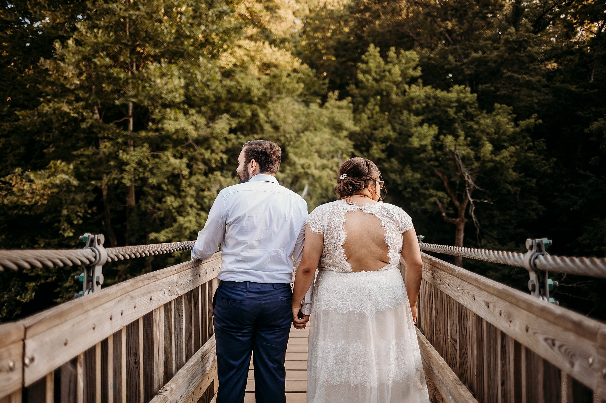 A man and a woman hold hands while on a suspension bridge over the water at their Turkey Run Elopement