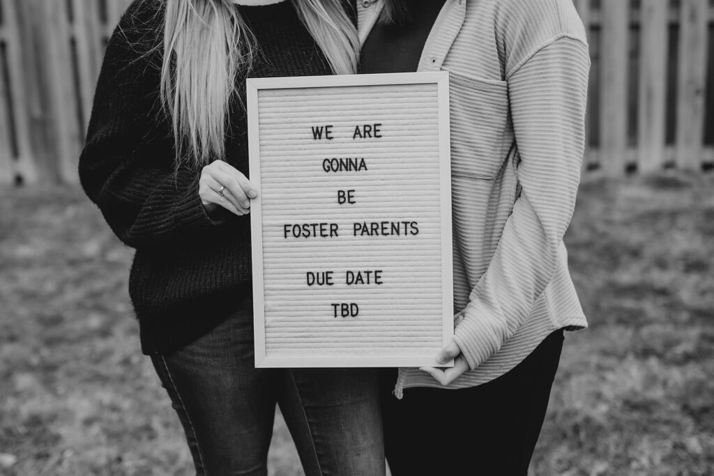 two women hold a sign that says "my siblings have paws" as they announce that they are becoming foster parents in indiana. 