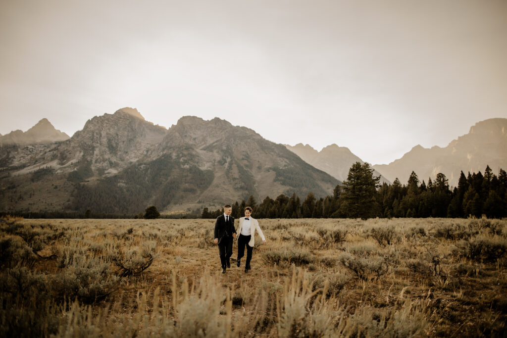 lgbtq+ couple, looking away from each other while holding hands in front of the grand tetons and deciding why eloping is the perfect choice for lgbtq+ couples. 